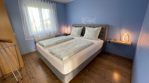 A bedroom with a bed, a window with sheer curtains, a bedside table with a lamp, and a wall sign. - Non-smoking vacation apartment 50sqm, no. 1, 2 bedrooms, max. 4 persons - (Rust)