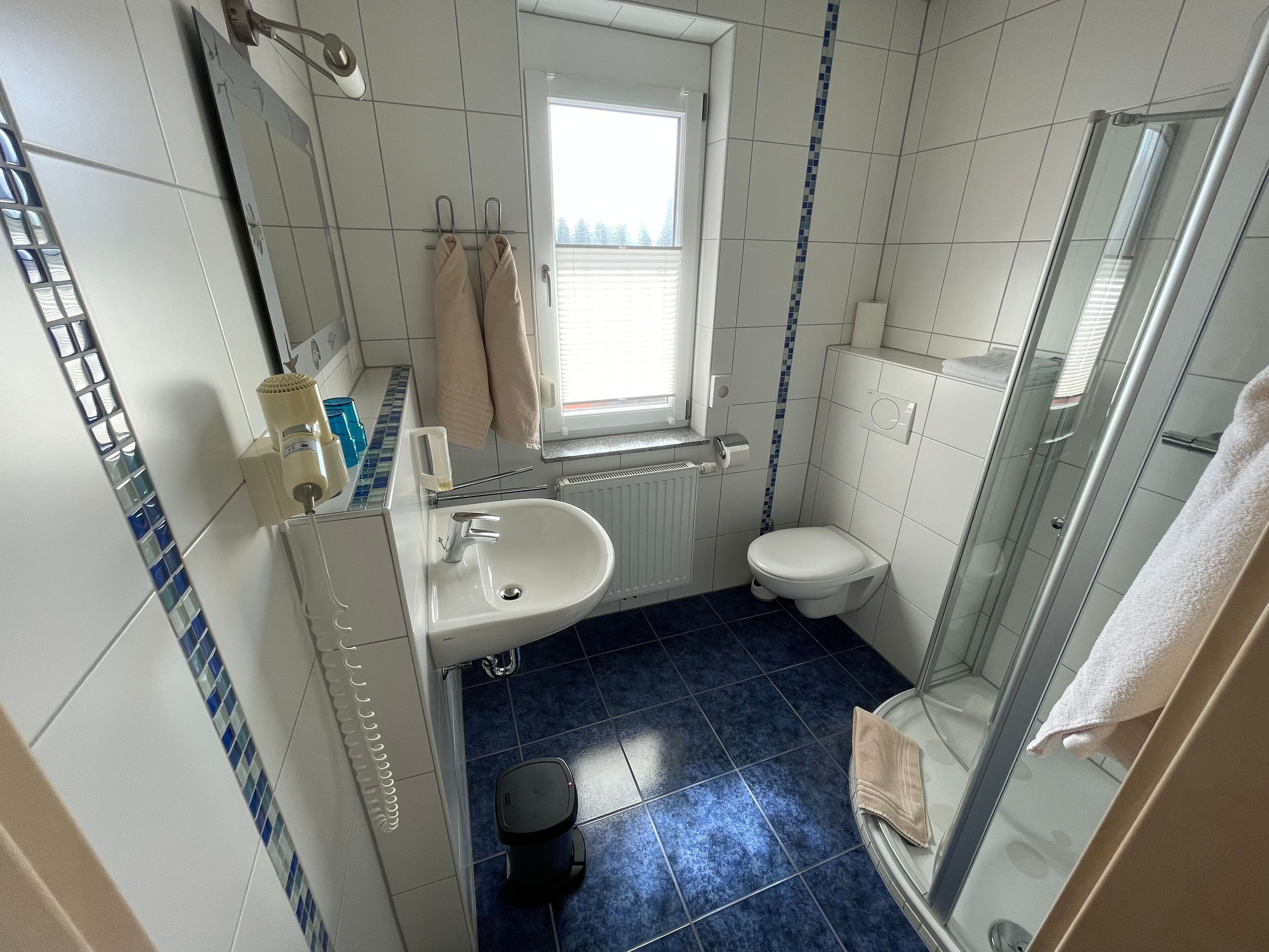 Et lille badeværelse med hvid vask, toilet og brusekabine i glas.