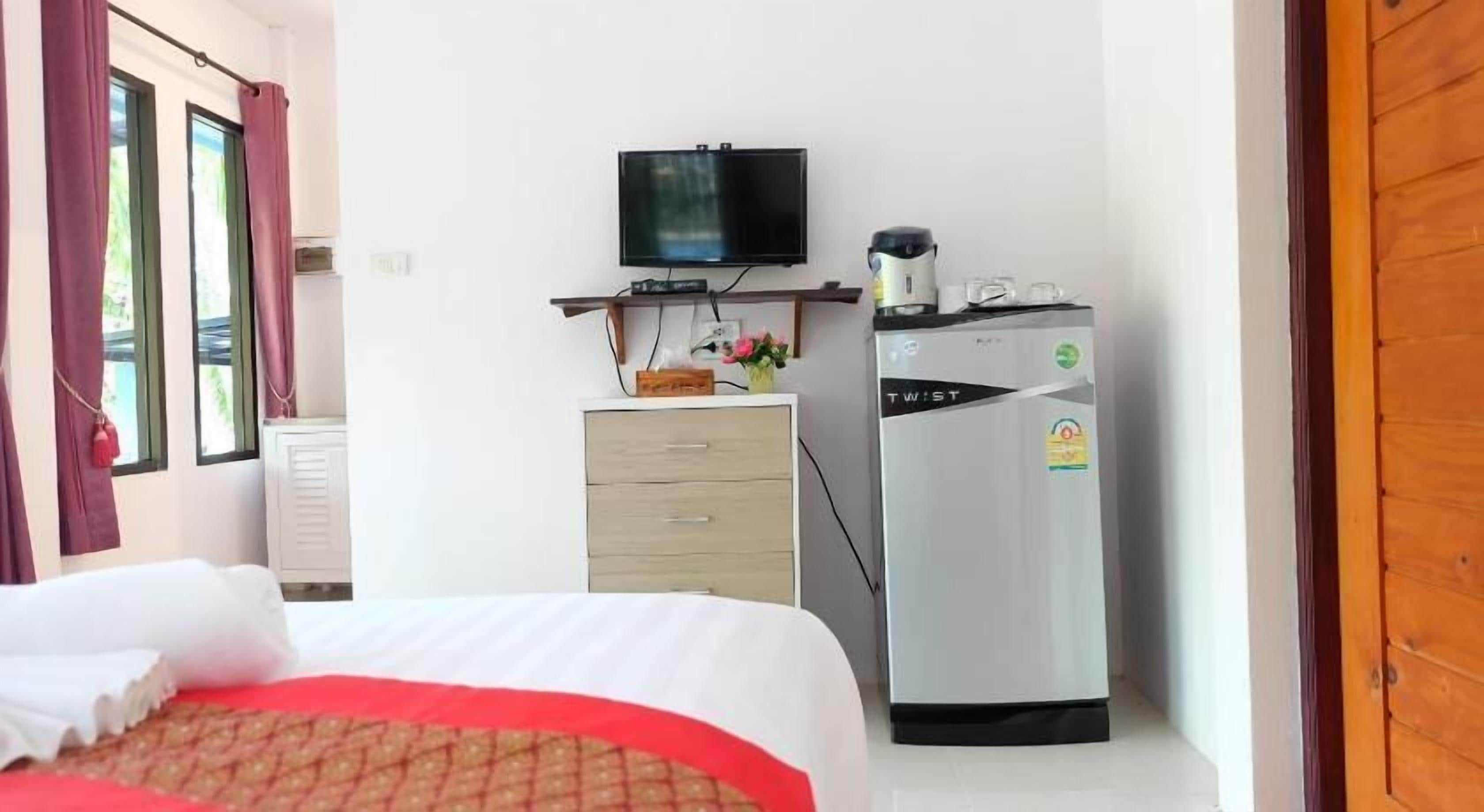 A hotel room with a bed, a TV, a coffee maker, and a refrigerator.