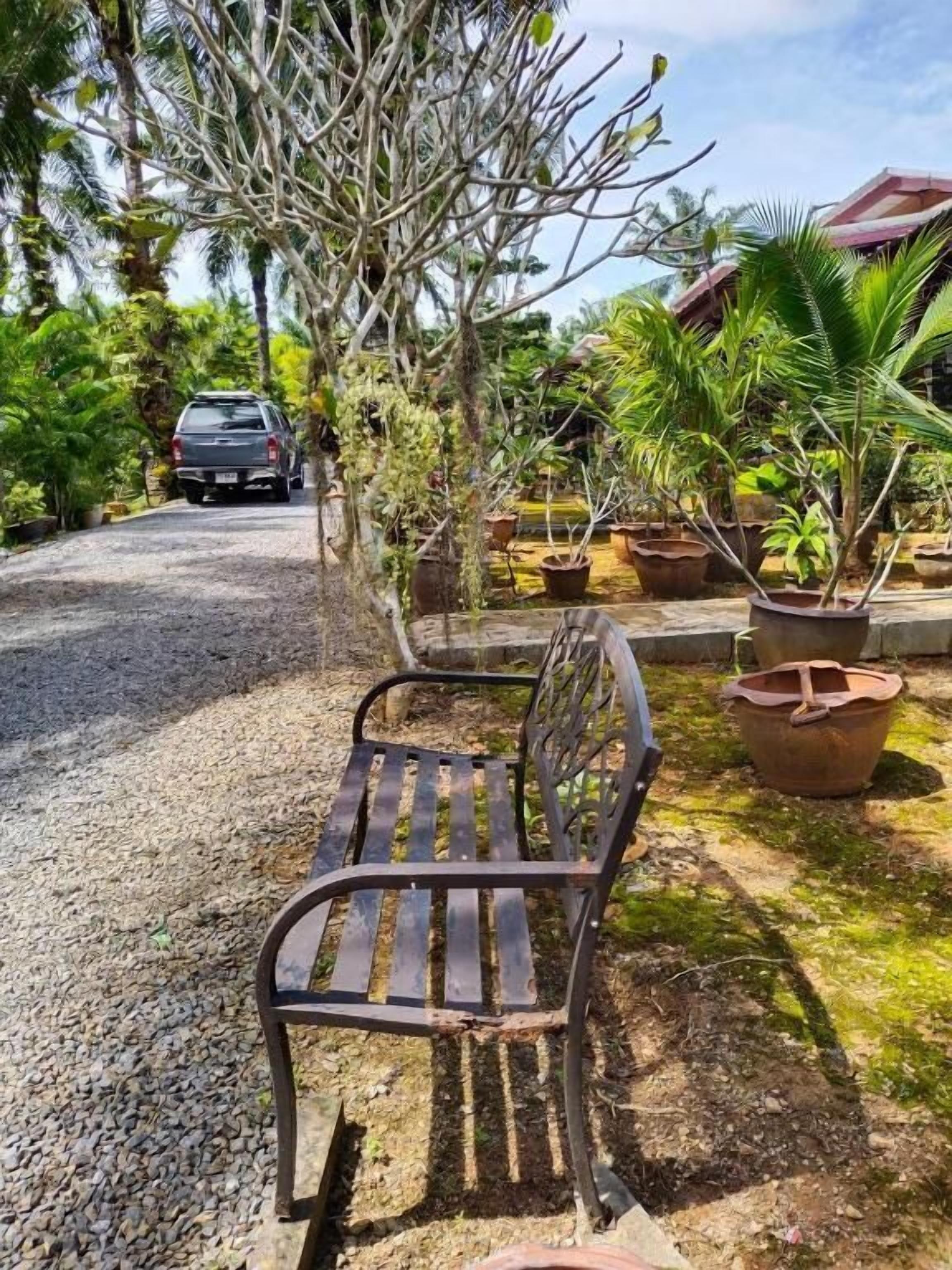 A gravel path leading to a bench surrounded by potted plants and a parked car.