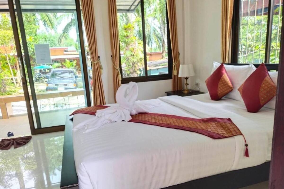 A hotel room with a bed, a nightstand, a lamp, and a view of greenery outside.
