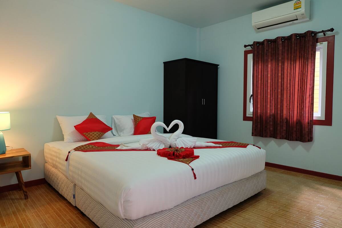 A hotel room with a bed, a wardrobe, a window with curtains, and an air conditioning unit.
