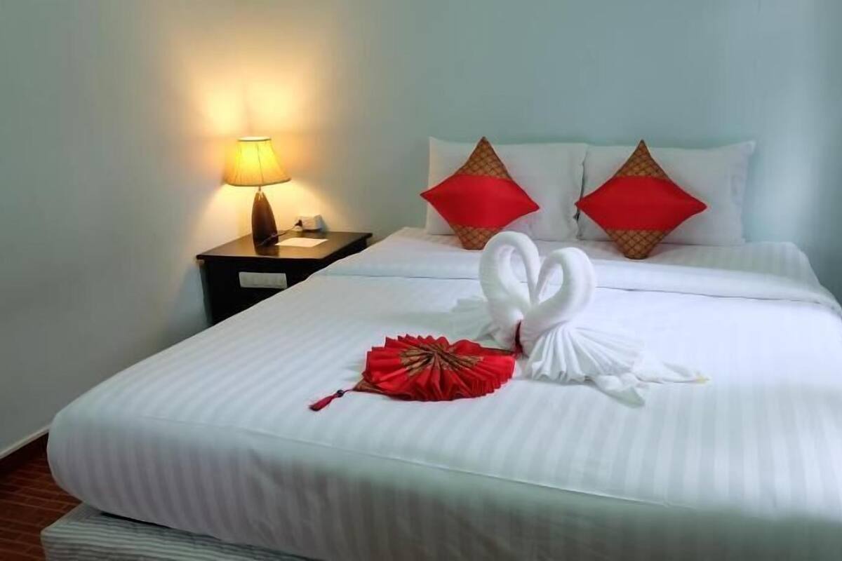 A hotel room with a neatly made bed, a bedside lamp, and two red decorative pillows.