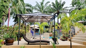 A covered outdoor seating area with lounge chairs, surrounded by lush tropical plants and a pool. - Palmthien Pool Villa Aonang (Krabi)