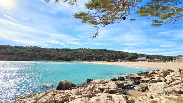 A coastal landscape with a rocky shoreline, clear turquoise waters, and a backdrop of green hills.