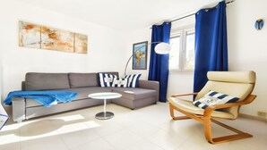 A living room with a grey sofa, a round coffee table, a blue chair, and a painting on the wall.