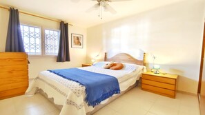 A bedroom with a bed, wooden nightstands, a ceiling fan, and a window with curtains.