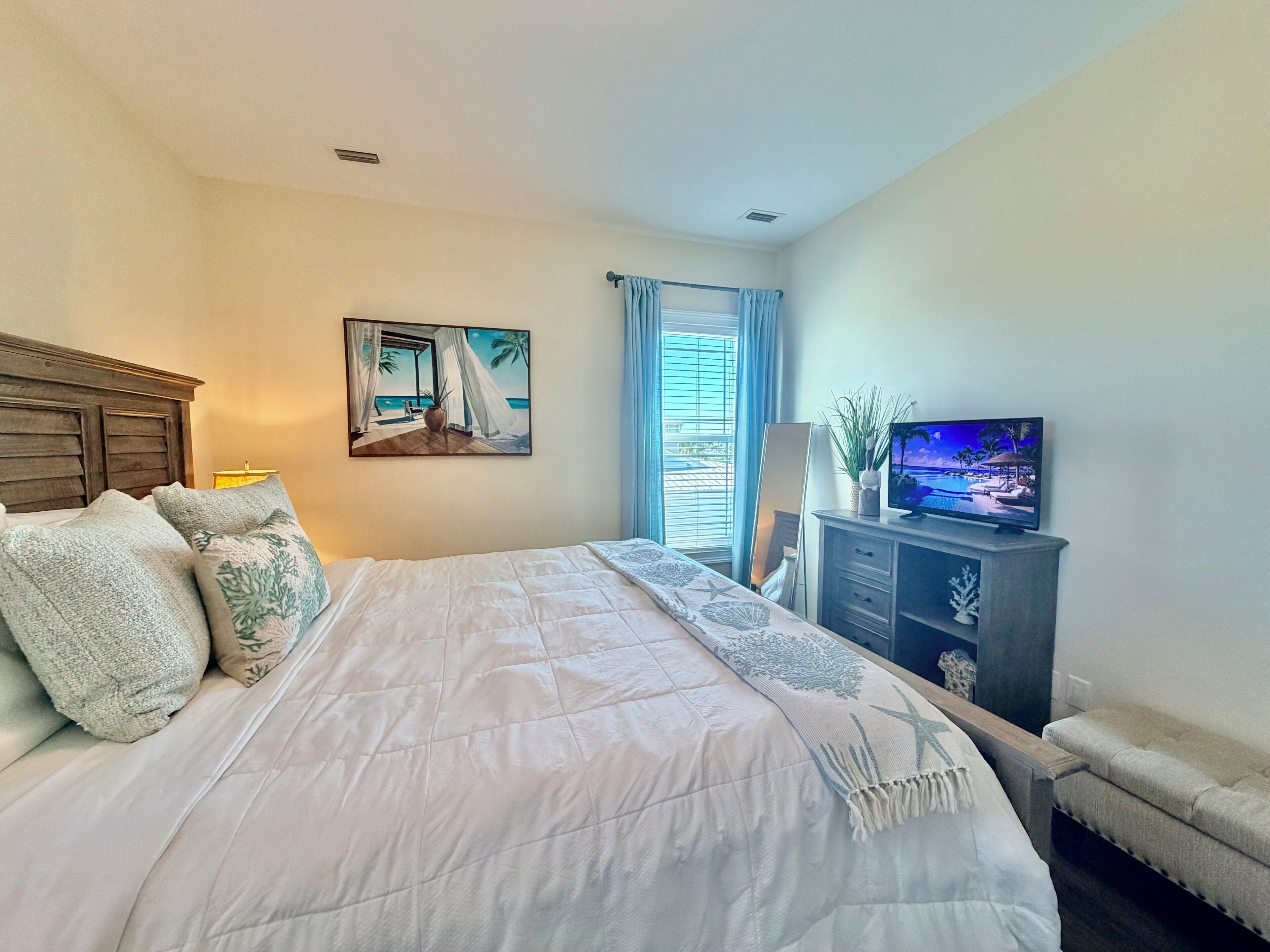 A bedroom with a bed, a painting, a TV, and a window with curtains.