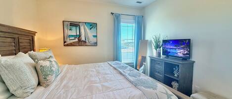 A bedroom with a bed, a painting, a TV, and a window with curtains.