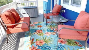 A balcony with two orange chairs and a small table, a colorful floral rug, and a view of the street. - Stylish space, 180ft to beach,parking (Point Pleasant Beach)