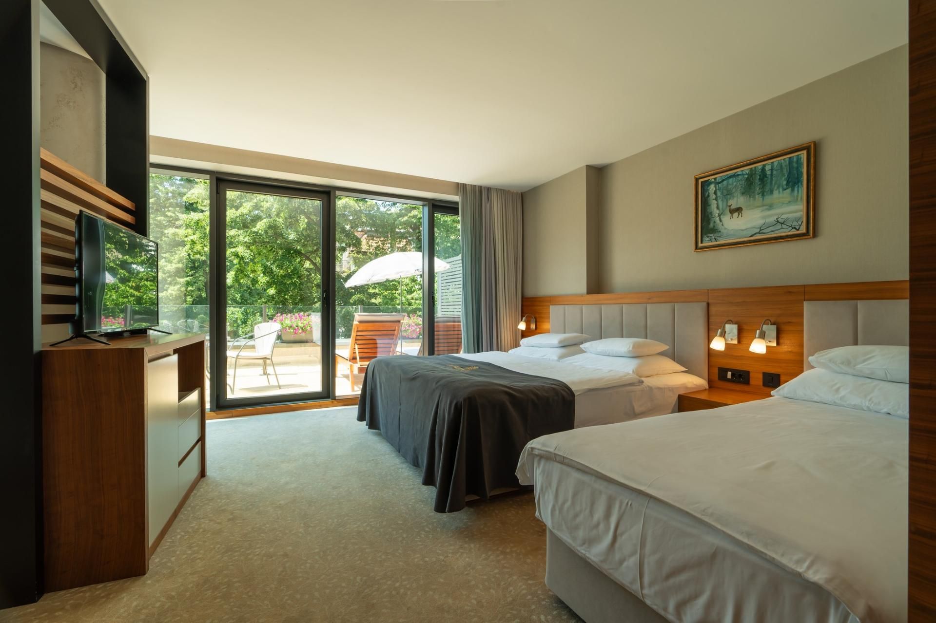 A hotel room with two beds, a TV, a painting, and a balcony with outdoor seating.