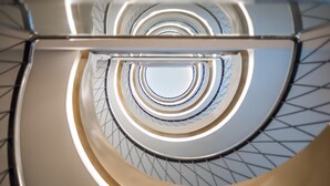 Een wenteltrap met een metalen en glazen ontwerp, voorzien van een geometrisch patroon op de muren en een centraal lichtarmatuur.