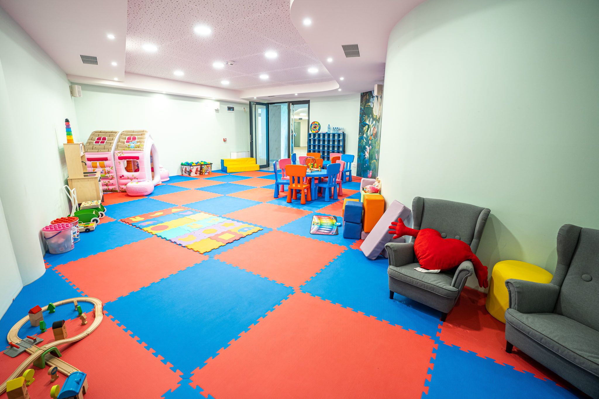A playroom with colorful mats, play structures, and seating.