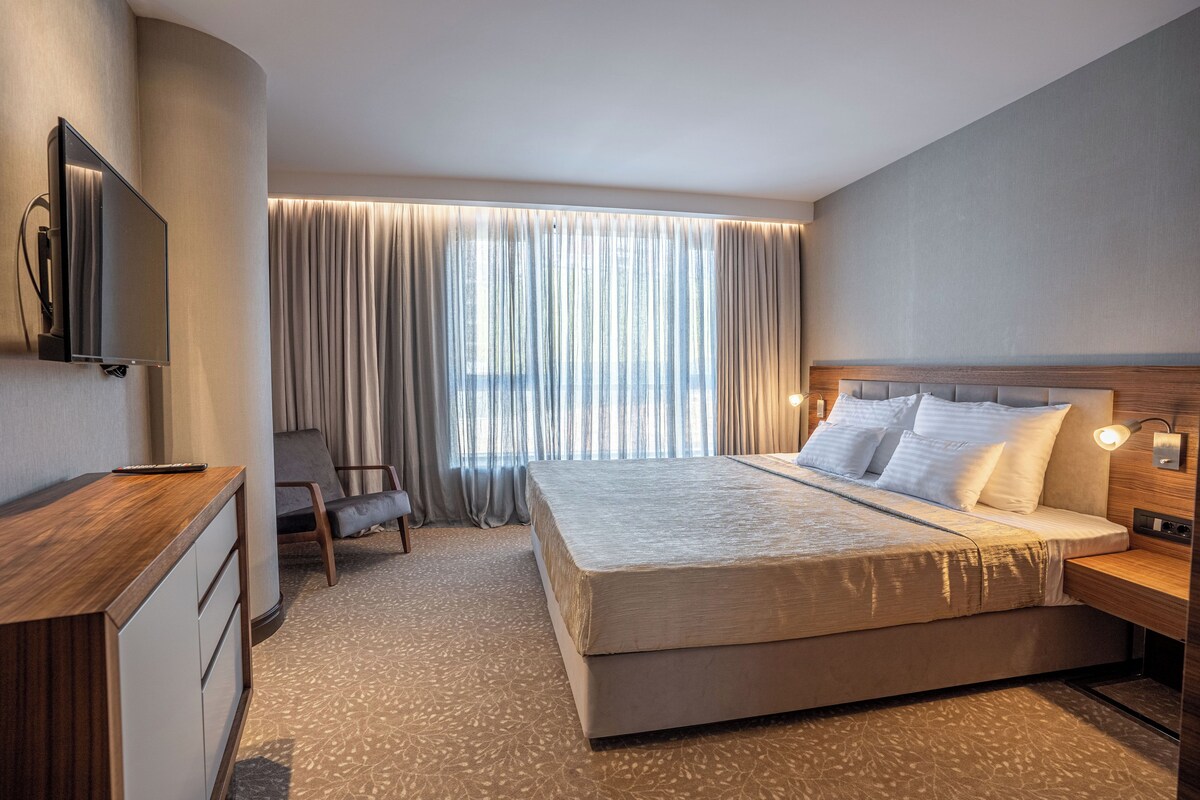 Una habitación de hotel moderna con una cama grande, un escritorio, una silla y un televisor.