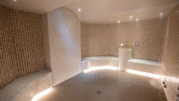 Relax in a serene spa room with a unique mosaic tile wall, curved bench, and soft ambient lighting.