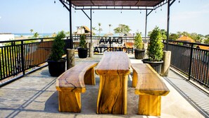 An outdoor wooden deck with picnic tables and potted plants, overlooking a beach and ocean.
