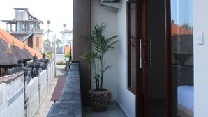 A narrow balcony with a potted plant, a bench, and a view of neighboring buildings. - Dana Homestay (Tibubeneng)