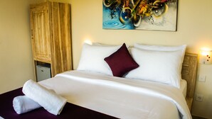 A hotel room with a bed, a wooden cabinet, a painting, and a night light. - Dana Homestay (Tibubeneng)