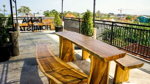 A wooden bench and table set on a concrete patio with a view of a cityscape and palm trees.