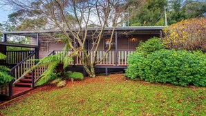 A two-story house with a covered porch, a staircase, and a well-maintained garden with various plants and trees.
