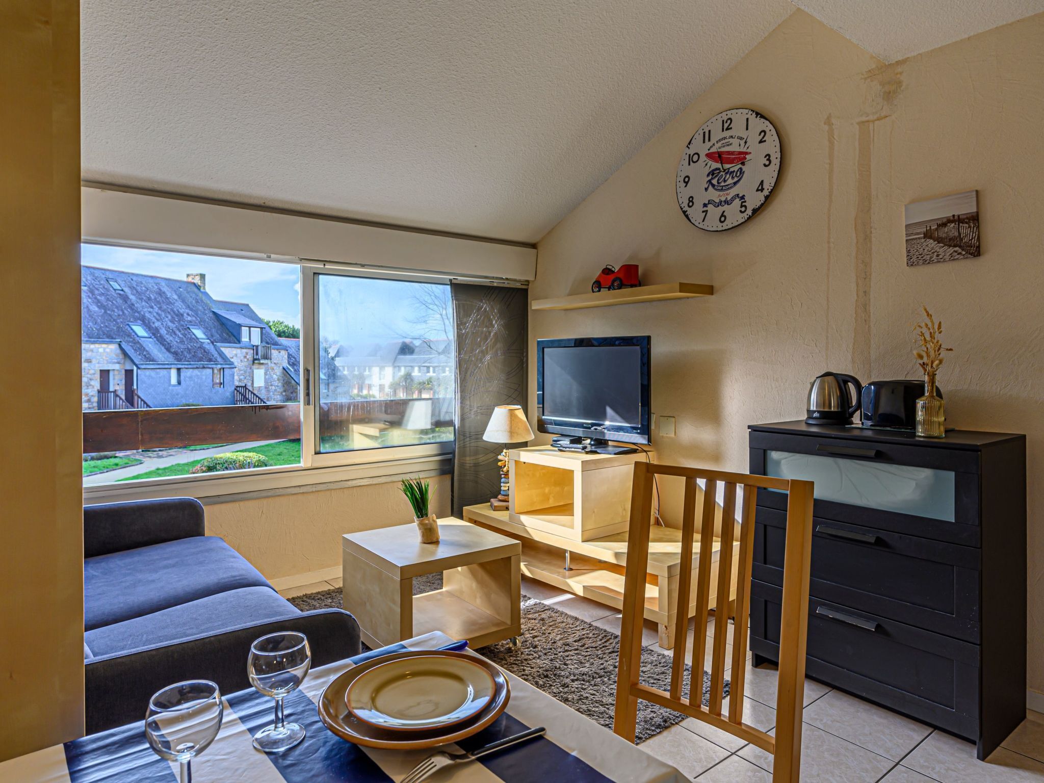 Ett kompakt vardagsrum med en soffa, ett matbord, en tv och en klocka på väggen.