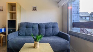 A living room with a grey sofa, a small table with a plant, a bookshelf, and a window with a view of buildings. - Maison Port En Dro by Interhome (Carnac)