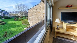 A balcony with a view of a green garden and houses, a wooden desk with a TV, and a lamp. - Maison Port En Dro by Interhome (Carnac)