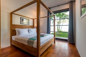 A four-poster bed with white bedding and a green patterned throw, a framed picture on the wall, and a view of greenery through a large window. - Seminyak, Large Groups, 11 Bdr/14 beds,Near Beach (Seminyak)