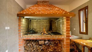 A brick-built fireplace with a chimney, a stack of firewood, and a window to the right.