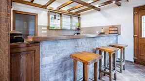 A kitchen with a wooden bar and stools, a stone backsplash, and a wooden ceiling with exposed beams.