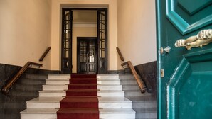 Portaat, joissa on marmorista tehdyt askelmat ja punainen matto, johtavat tummaan puuoveen, jossa on lasiruudut.