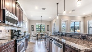 A modern kitchen with dark wood cabinets, stainless steel appliances, granite countertops, and pendant lighting. - Pet Friendly ~ Two Golf Carts ~ Golf Course View (Miramar Beach)