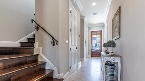 A hallway with a wooden staircase, white doors, a decorative wall piece, and a trash can. - Pet Friendly ~ Two Golf Carts ~ Golf Course View (Miramar Beach)