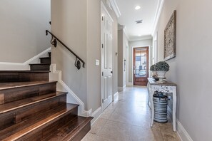 A hallway with a wooden staircase, white doors, a decorative wall piece, and a trash can. - Pet Friendly ~ Two Golf Carts ~ Golf Course View (Miramar Beach)