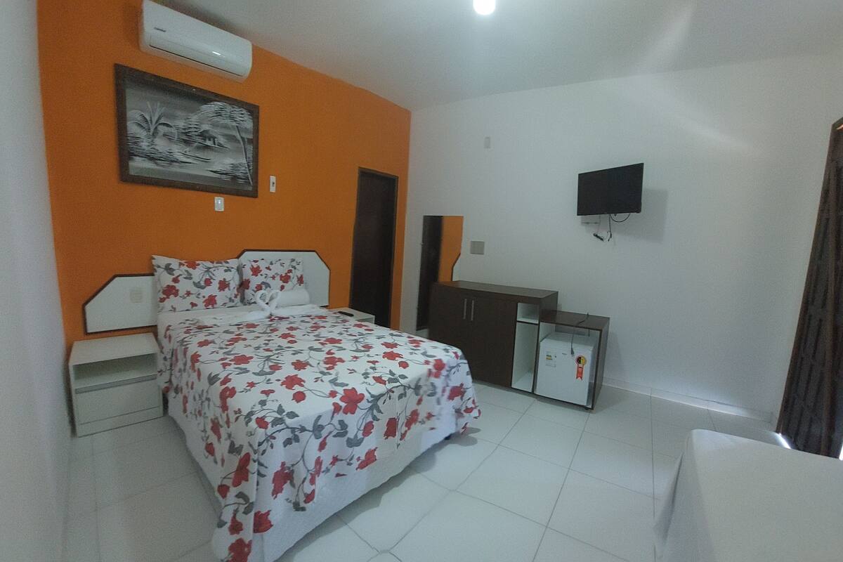 A bedroom with a bed, a dresser, a TV, and an air conditioner.