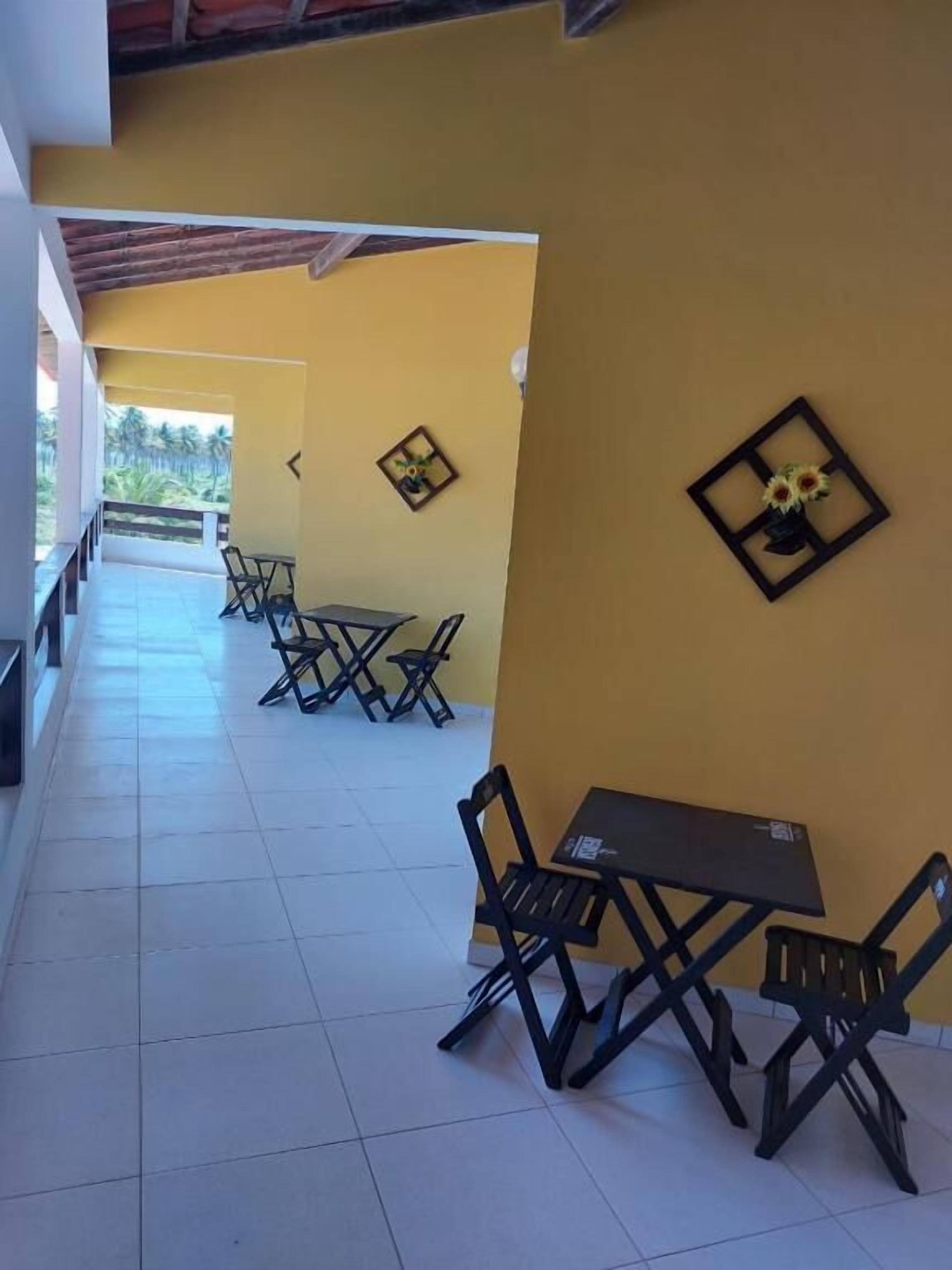 An outdoor seating area with tables and chairs, a yellow wall, and framed artwork.