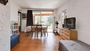 Habitación pequeña con mesa de comedor, sillas, televisor, cama y una estantería.