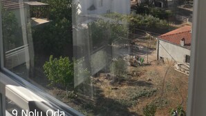 Vista desde una ventana sobre un pueblo costero con edificios, vegetación y cielo despejado.