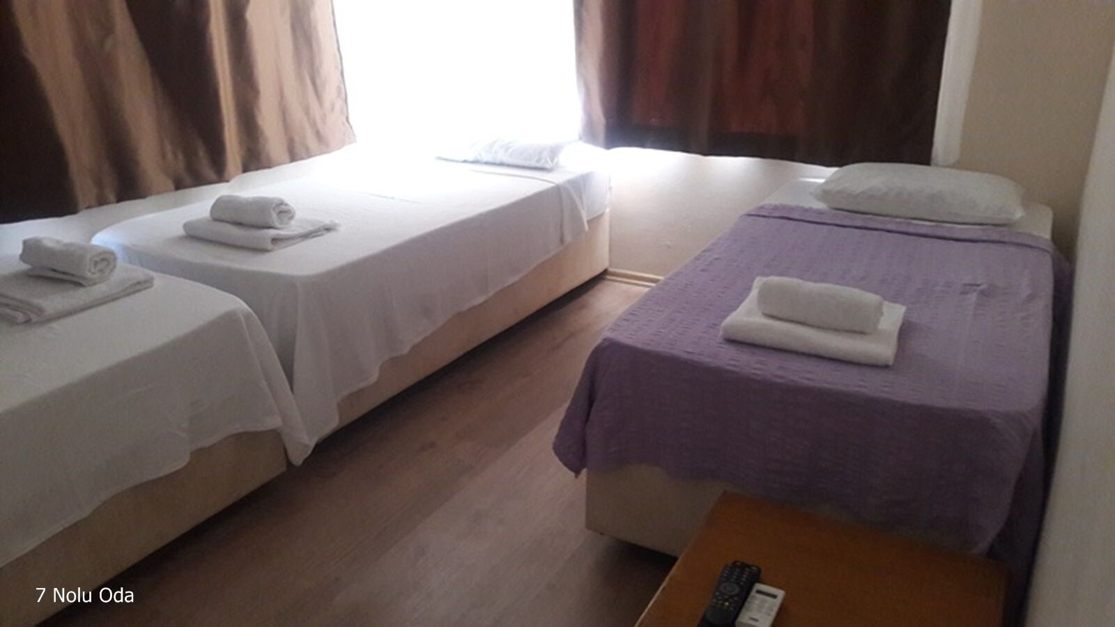 Une chambre d’hôtel avec deux lits simples, chacun recouvert d’une courtepointe blanche et violette, et une table de chevet en bois avec une télécommande.