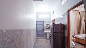 Ein schmaler Flur führt zu einem Schlafzimmer mit einem Bett, einem Kühlschrank und einem kleinen Waschbecken.