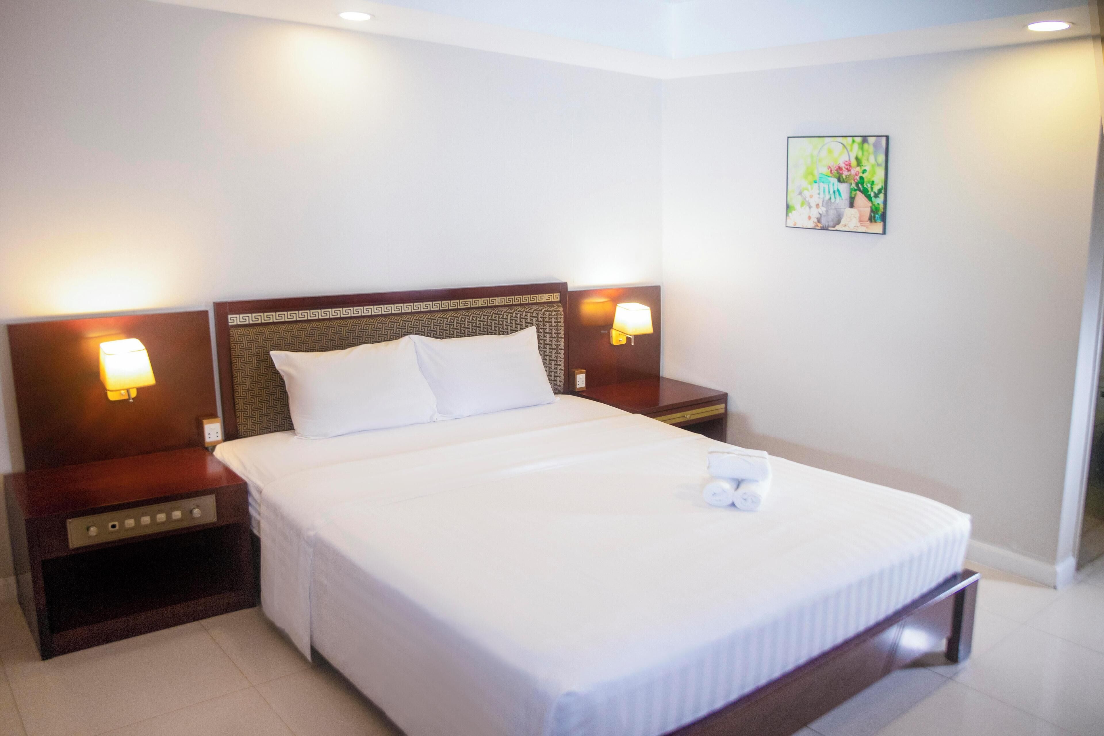 A neatly made bed with white linens, two bedside tables with lamps, and a painting on the wall.