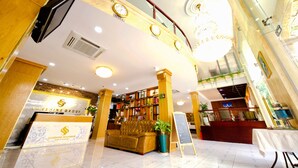 A reception area with a sofa, a bookshelf, a signboard, and a reception desk.