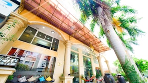 A hotel entrance with a red carpet, outdoor seating, palm trees, and a glass facade.
