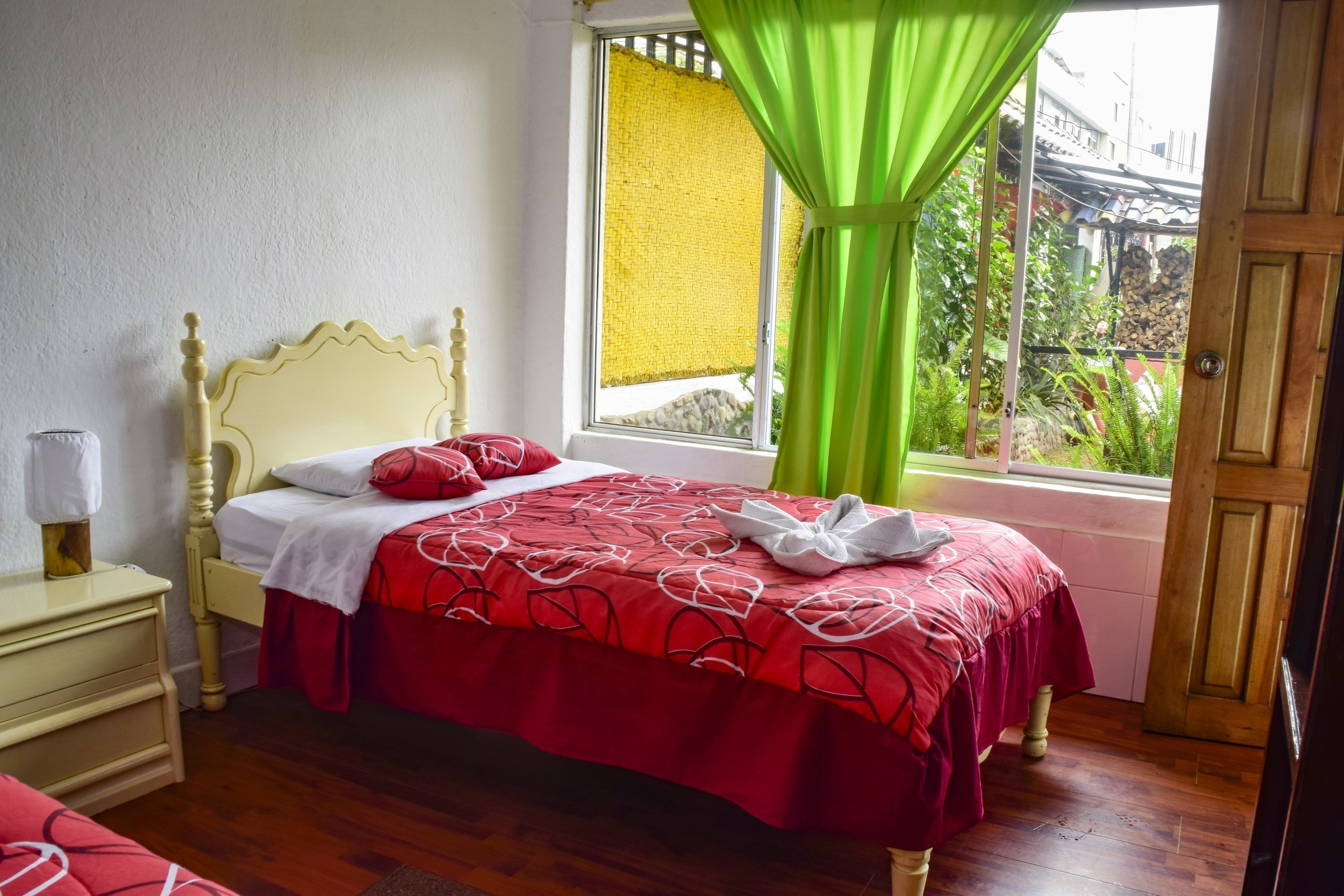 Un dormitorio con cama, mesita de noche, ventana con cortinas y vista a la vegetación.