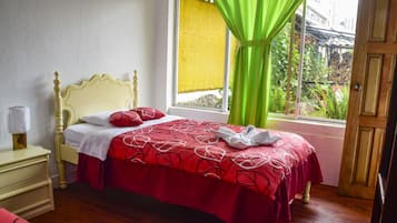 Un dormitorio con cama, mesita de noche, ventana con cortinas y vista a la vegetación.