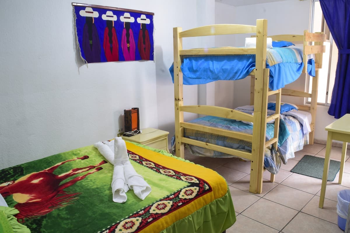 A room with a bunk bed, a bed with a colorful blanket, a small bedside table, and a wall decoration.