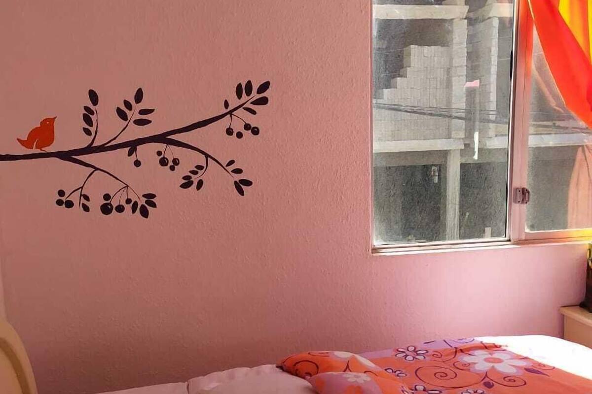 A bedroom with a bed, a window with curtains, and a wall decoration of a branch with leaves and a bird.