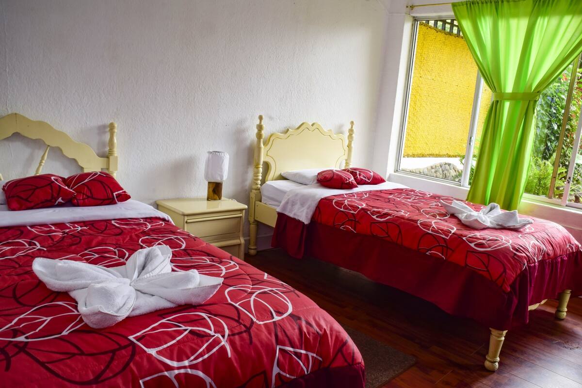 A hotel room with two beds, each with a red and white patterned bedspread, a wooden headboard, and a nightstand with a lamp.
