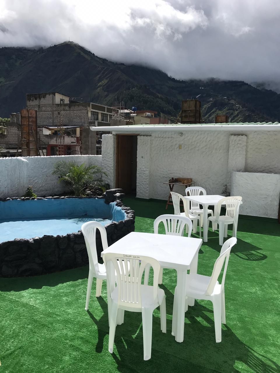 Una terraza en la azotea con piscina, sillas y mesas de plástico blanco.