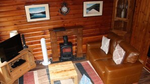 Interior acogedor de una cabaña de troncos con un mueble de televisión de madera, chimenea, sofá de cuero y alfombra estampada.